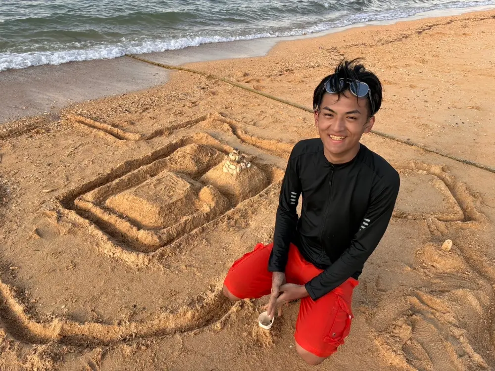 神保想叶さん。砂浜で、砂でつくった城の横にしゃがんで笑っている。